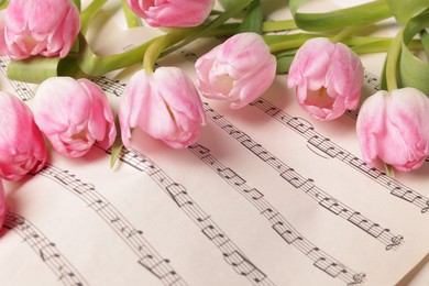 Photo of Beautiful tulips on sheet with music notes, closeup