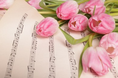 Photo of Beautiful tulips on sheet with music notes, closeup