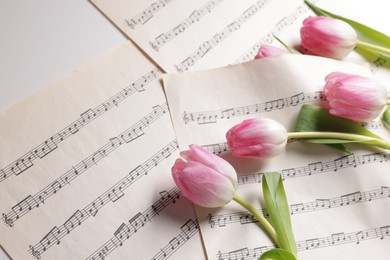 Photo of Beautiful tulips and sheets with music notes on white table, above view