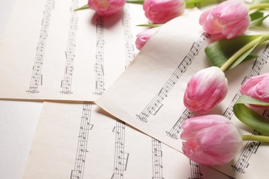 Photo of Beautiful tulips and sheets with music notes on white table, closeup