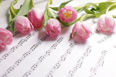 Photo of Beautiful tulips on sheets with music notes, closeup