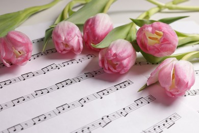 Photo of Beautiful tulips on sheets with music notes, closeup