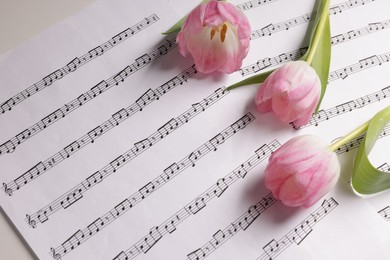 Photo of Beautiful tulips and sheets with music notes on white table, above view