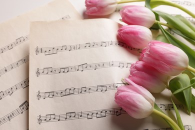 Photo of Beautiful tulips and sheets with music notes on white table, closeup