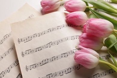 Photo of Beautiful tulips and sheets with music notes on white table, closeup