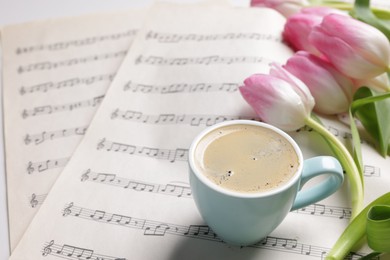 Photo of Beautiful tulips, cup of coffee and sheets with music notes on white table, closeup