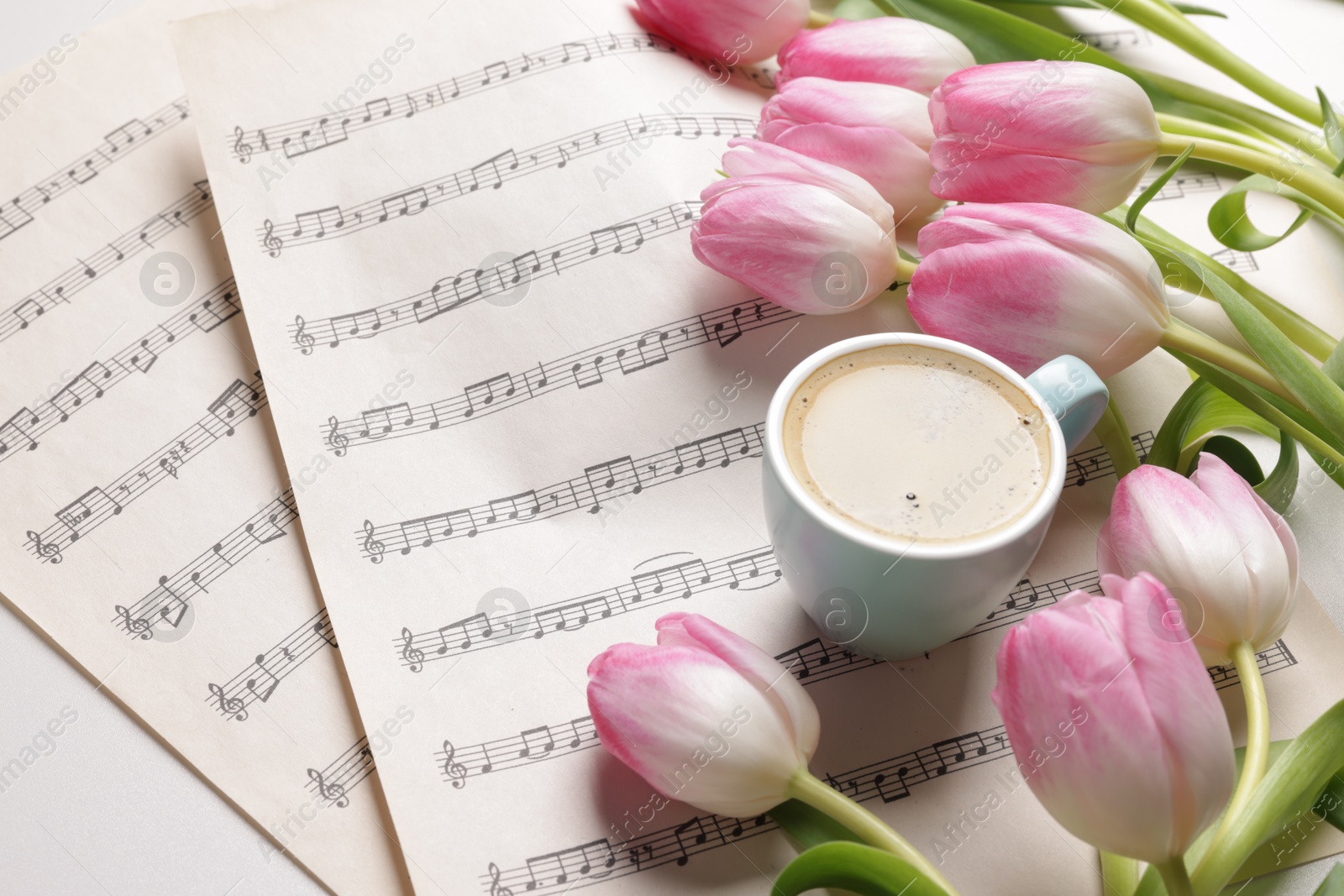 Photo of Beautiful tulips, cup of coffee and sheets with music notes on white table, closeup