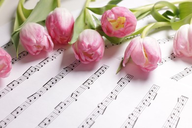 Photo of Beautiful tulips and sheets with music notes on white table, closeup