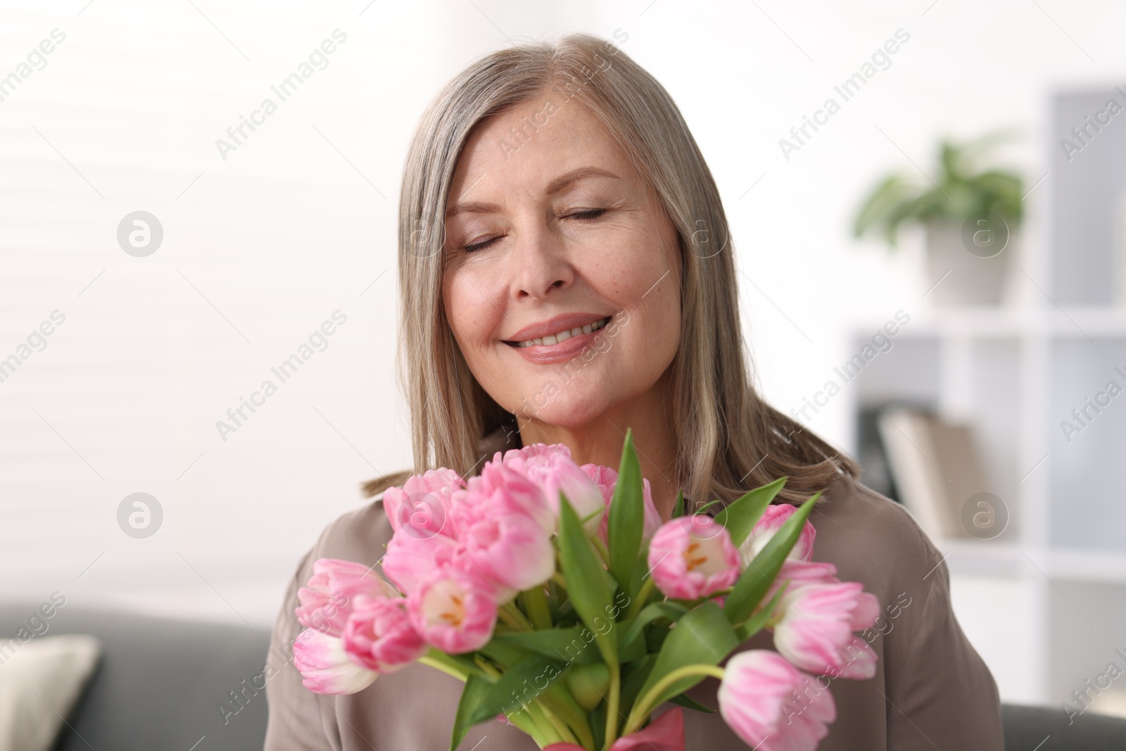 Photo of Smiling woman with bouquet of tulips at home