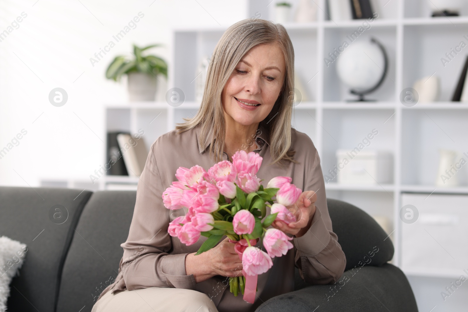 Photo of Smiling woman with bouquet of tulips on sofa at home