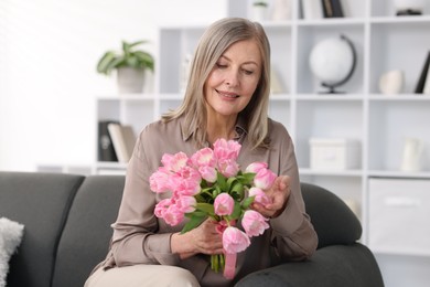 Photo of Smiling woman with bouquet of tulips on sofa at home