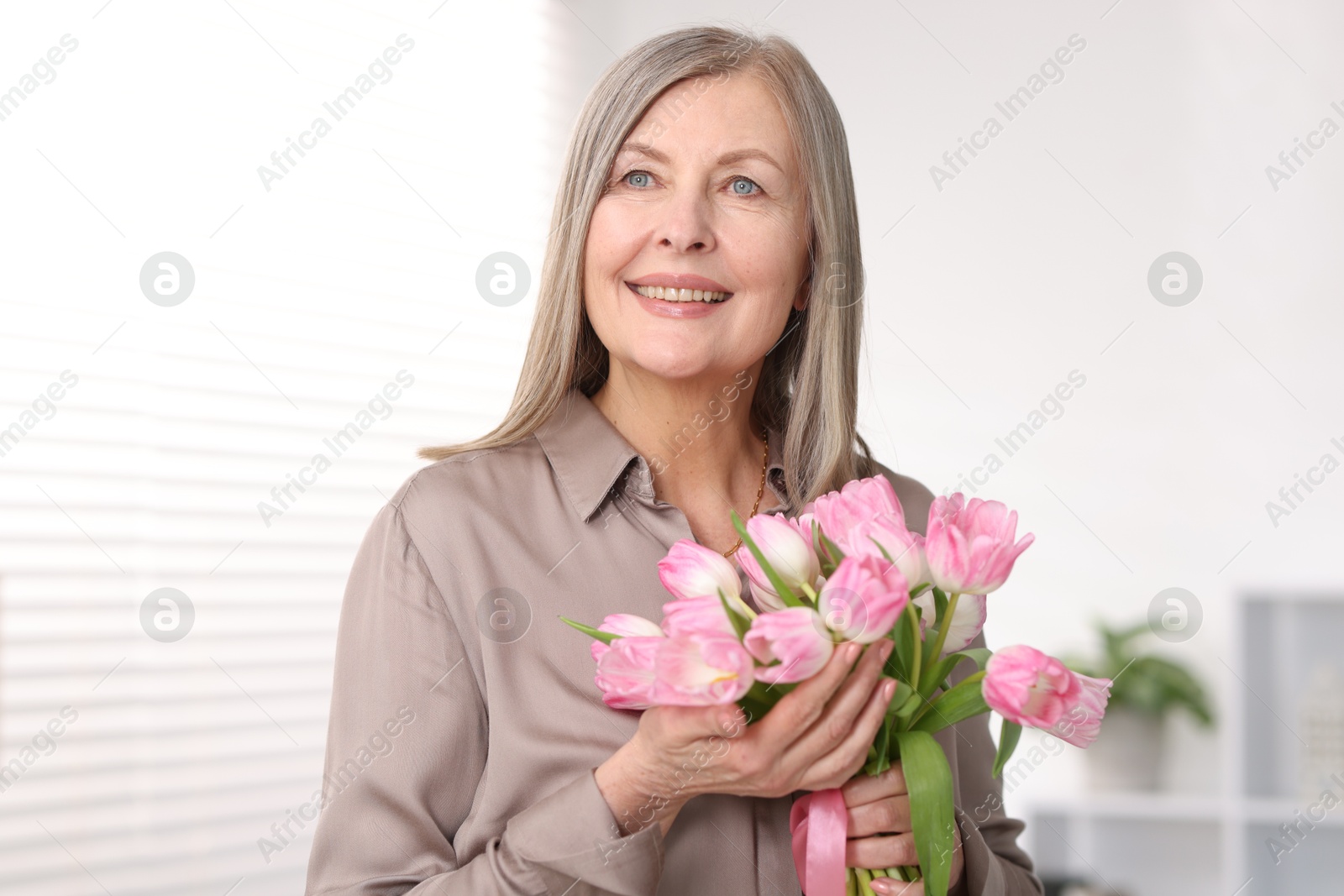 Photo of Smiling woman with bouquet of tulips at home