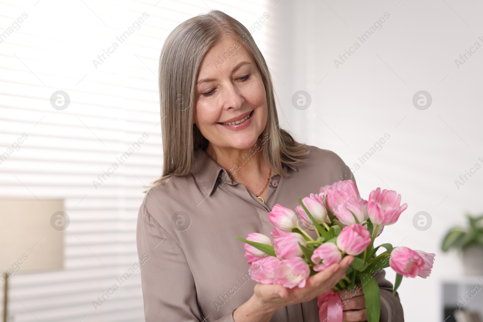 Photo of Smiling woman with bouquet of tulips at home