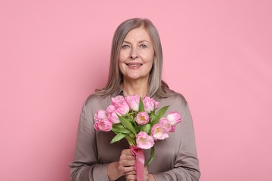 Photo of Smiling woman with bouquet of tulips on pink background