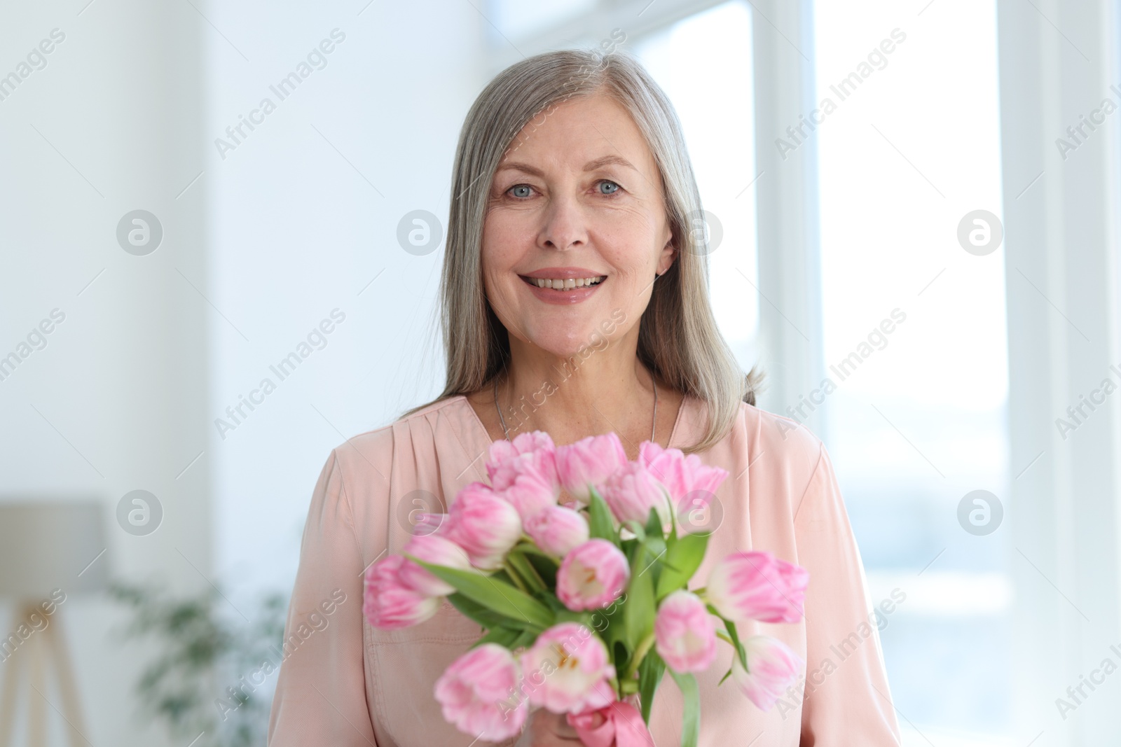 Photo of Smiling woman with bouquet of tulips at home