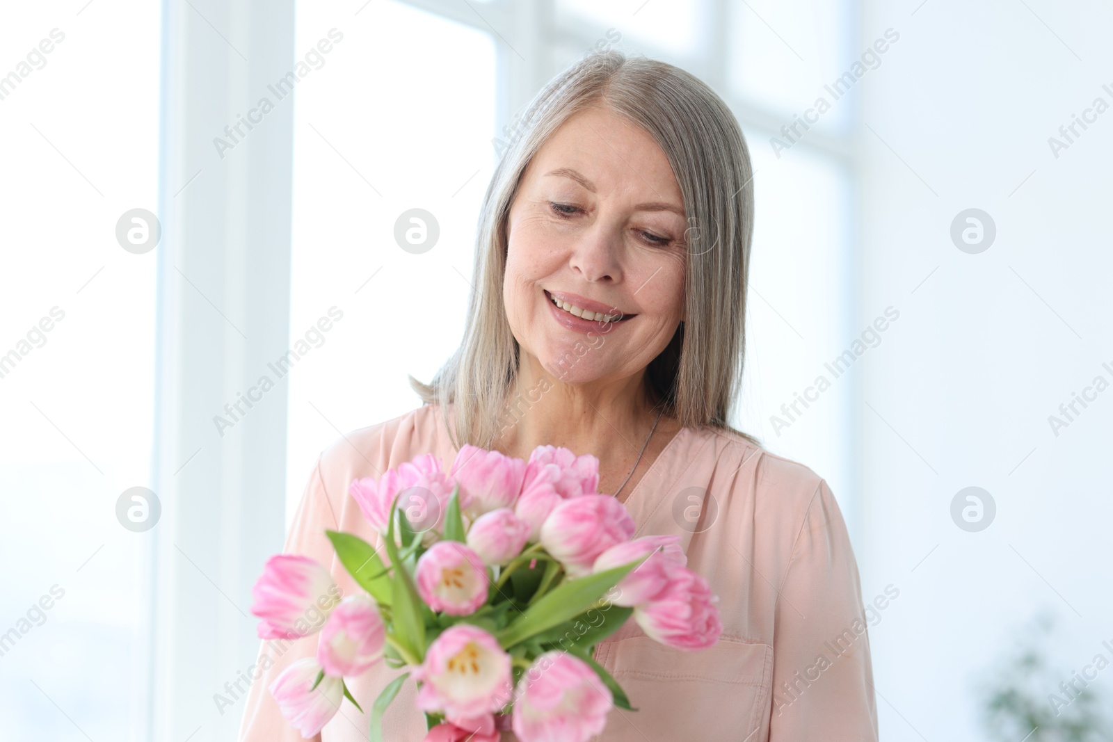 Photo of Smiling woman with bouquet of tulips at home