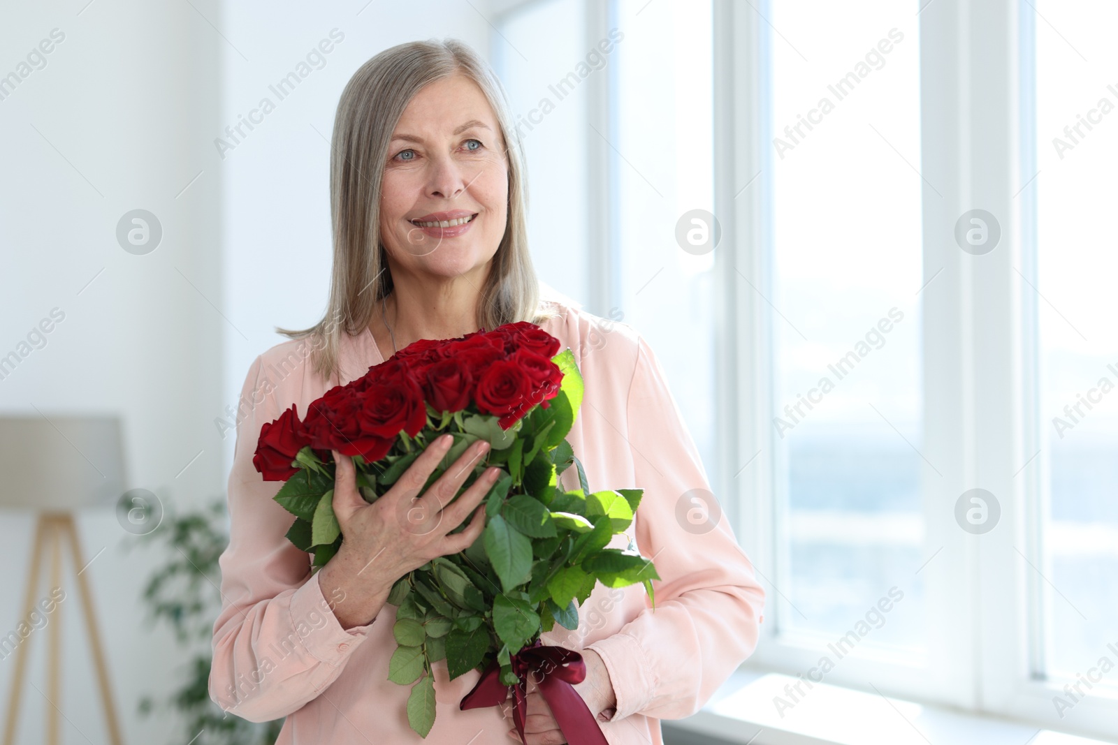 Photo of Smiling woman with bouquet of roses at home. Space for text