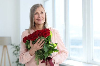 Photo of Smiling woman with bouquet of roses at home. Space for text