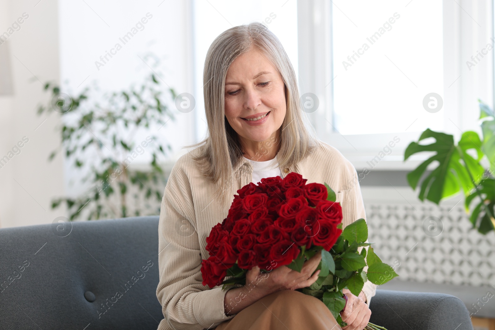 Photo of Smiling woman with bouquet of roses on sofa at home