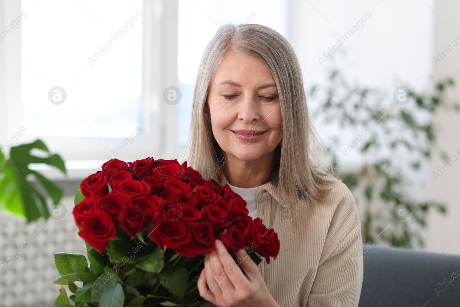 Photo of Smiling woman with bouquet of roses at home