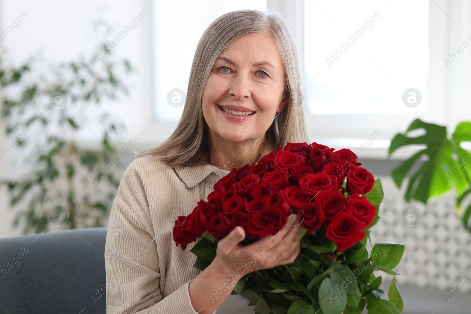 Photo of Smiling woman with bouquet of roses at home