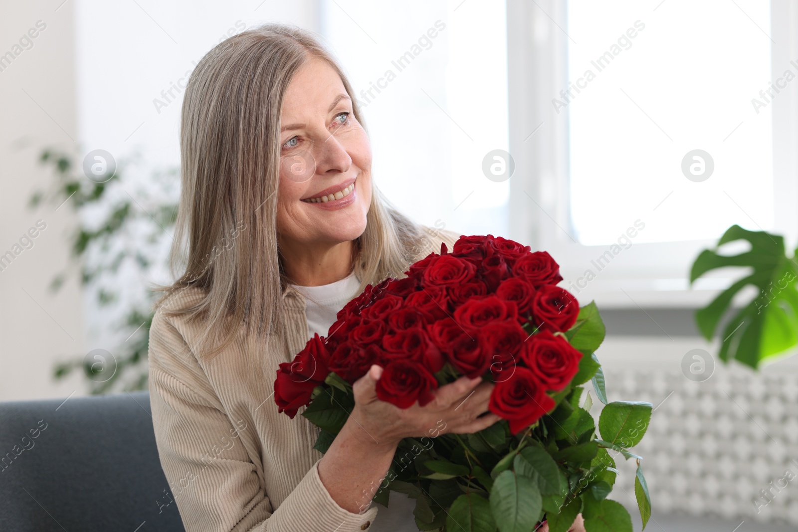 Photo of Smiling woman with bouquet of roses on sofa at home