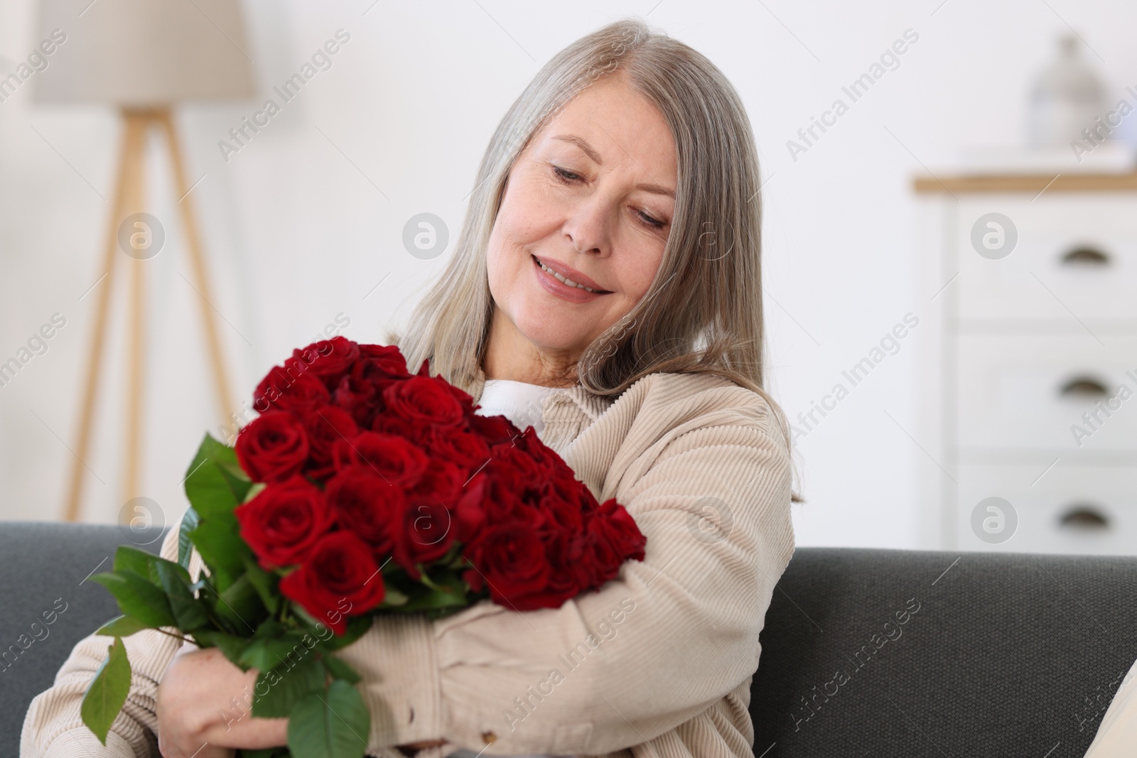 Photo of Smiling woman with bouquet of roses on sofa at home