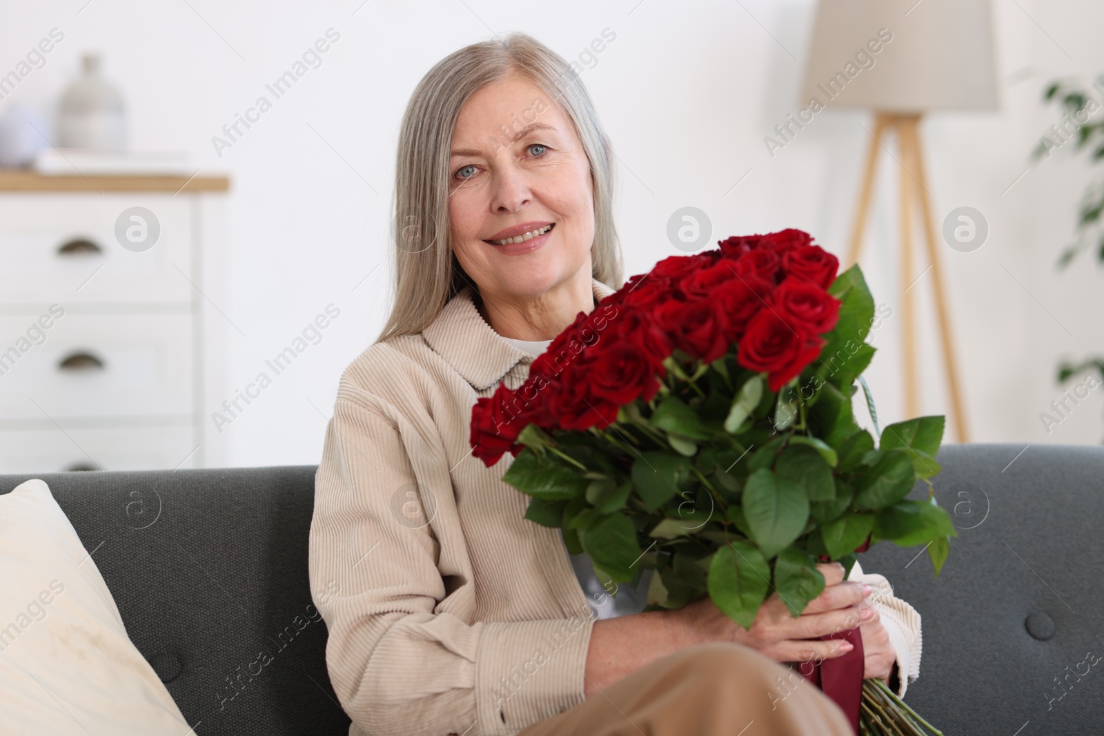 Photo of Smiling woman with bouquet of roses on sofa at home