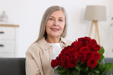 Photo of Smiling woman with bouquet of roses on sofa at home