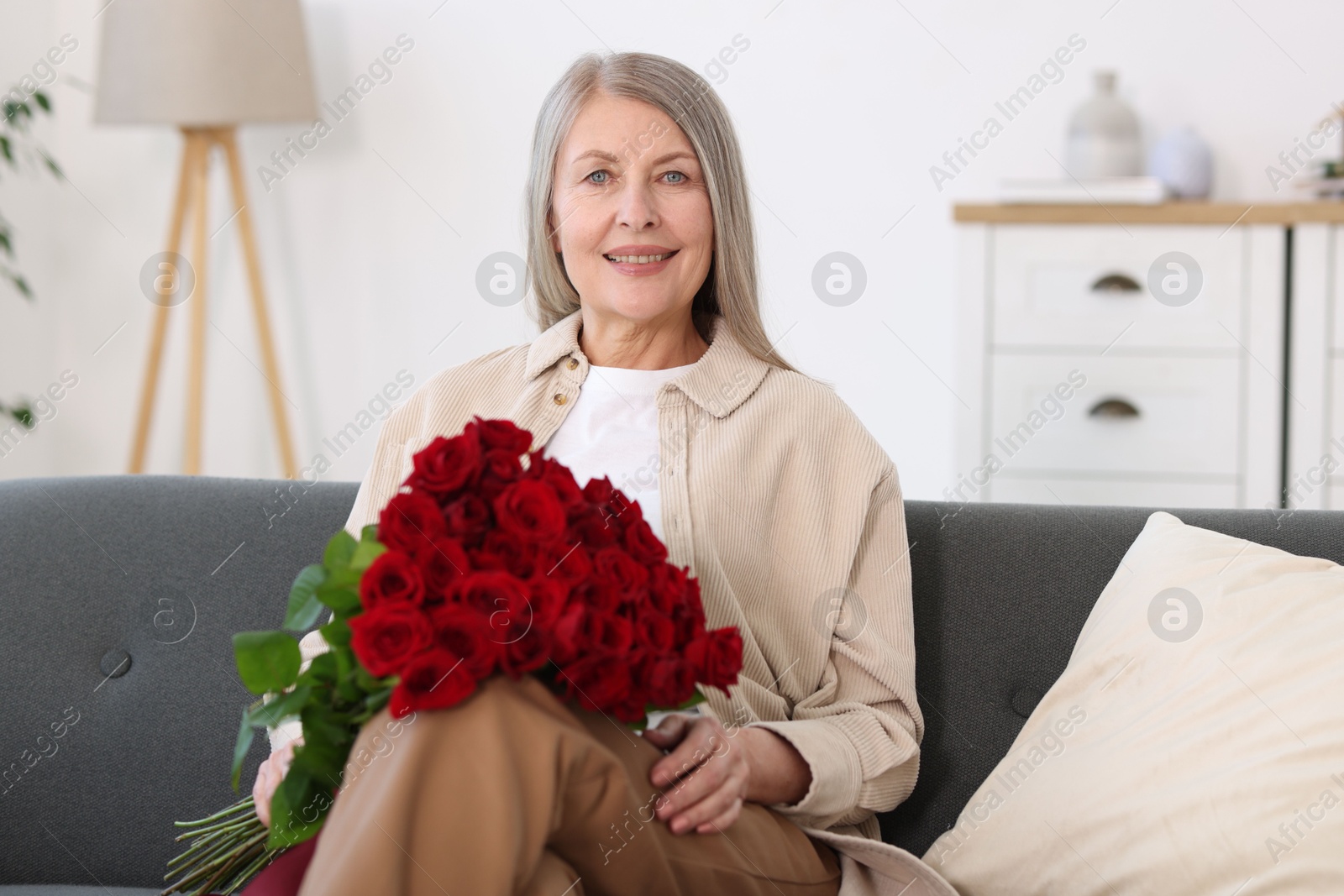 Photo of Smiling woman with bouquet of roses on sofa at home