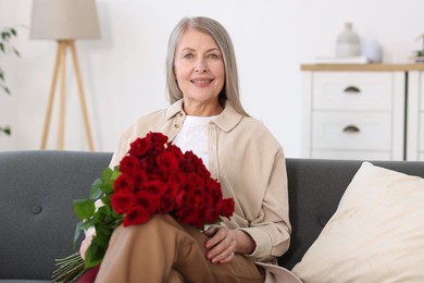 Smiling woman with bouquet of roses on sofa at home