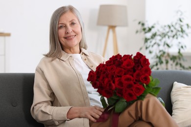 Smiling woman with bouquet of roses on sofa at home