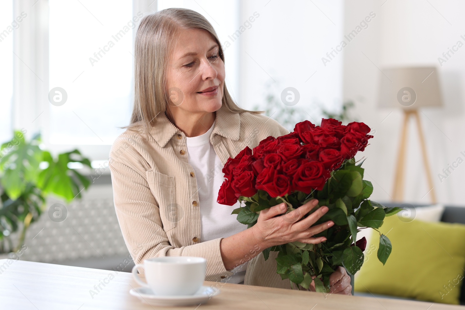 Photo of Beautiful woman with bouquet of roses at table indoors