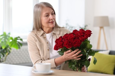 Photo of Beautiful woman with bouquet of roses at table indoors