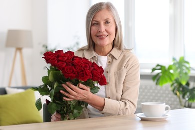 Smiling woman with bouquet of roses at table indoors