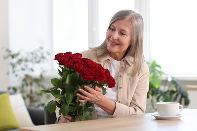 Smiling woman with bouquet of roses at table indoors