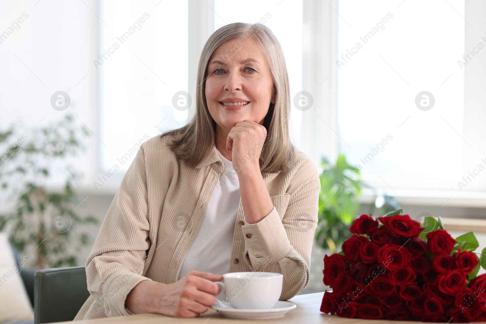 Photo of Smiling woman with bouquet of roses drinking at table indoors