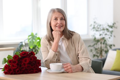 Photo of Smiling woman with bouquet of roses drinking at table indoors