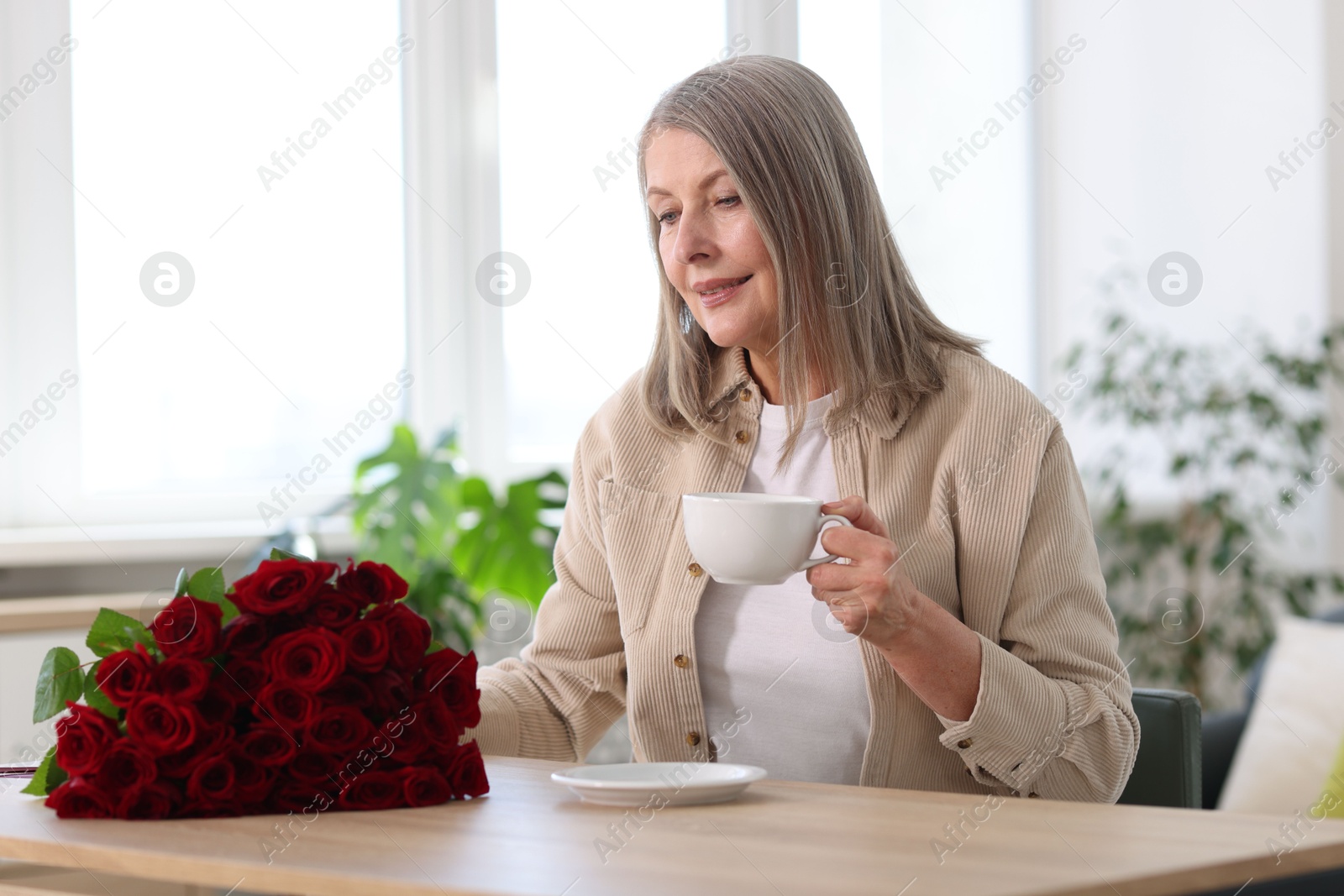 Photo of Smiling woman with bouquet of roses at table indoors