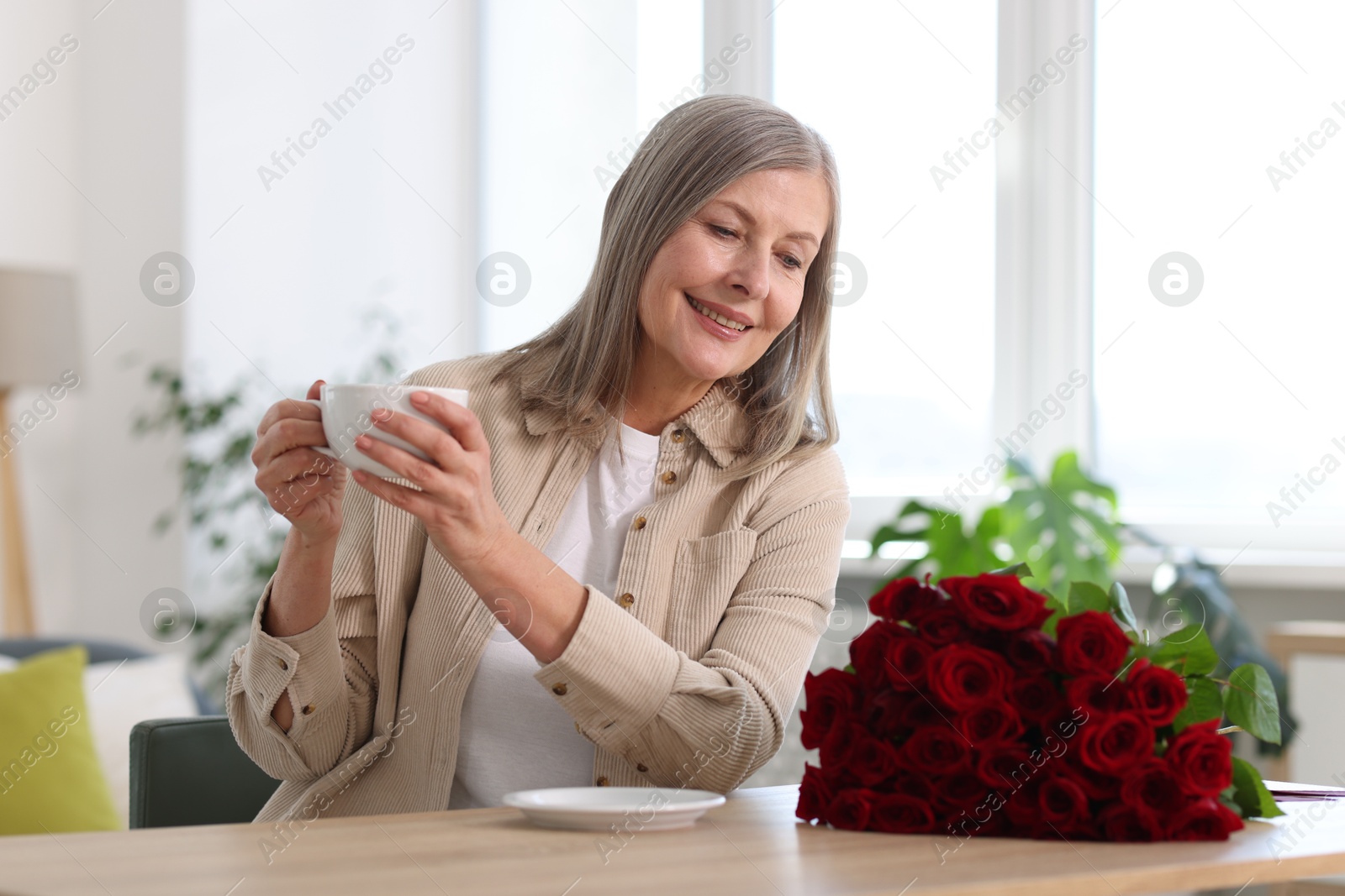 Photo of Smiling woman with bouquet of roses drinking at table indoors