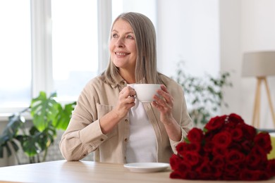 Photo of Smiling woman with bouquet of roses drinking at table indoors