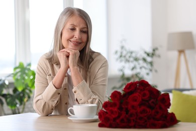 Photo of Smiling woman with bouquet of roses at table indoors