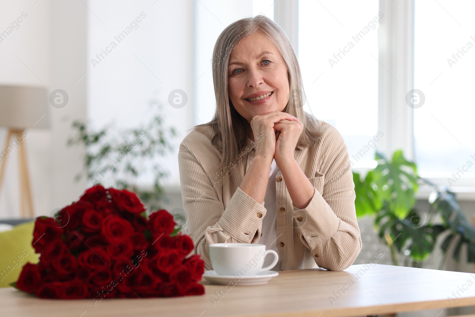 Photo of Smiling woman with bouquet of roses at table indoors