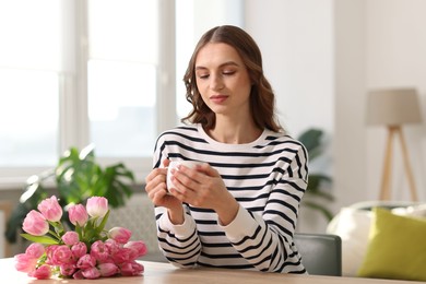 Photo of Smiling woman with bouquet of tulips drinking at table indoors