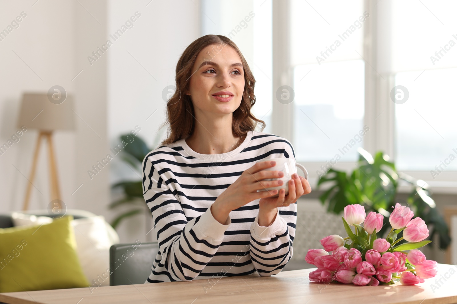 Photo of Smiling woman with bouquet of tulips drinking at table indoors