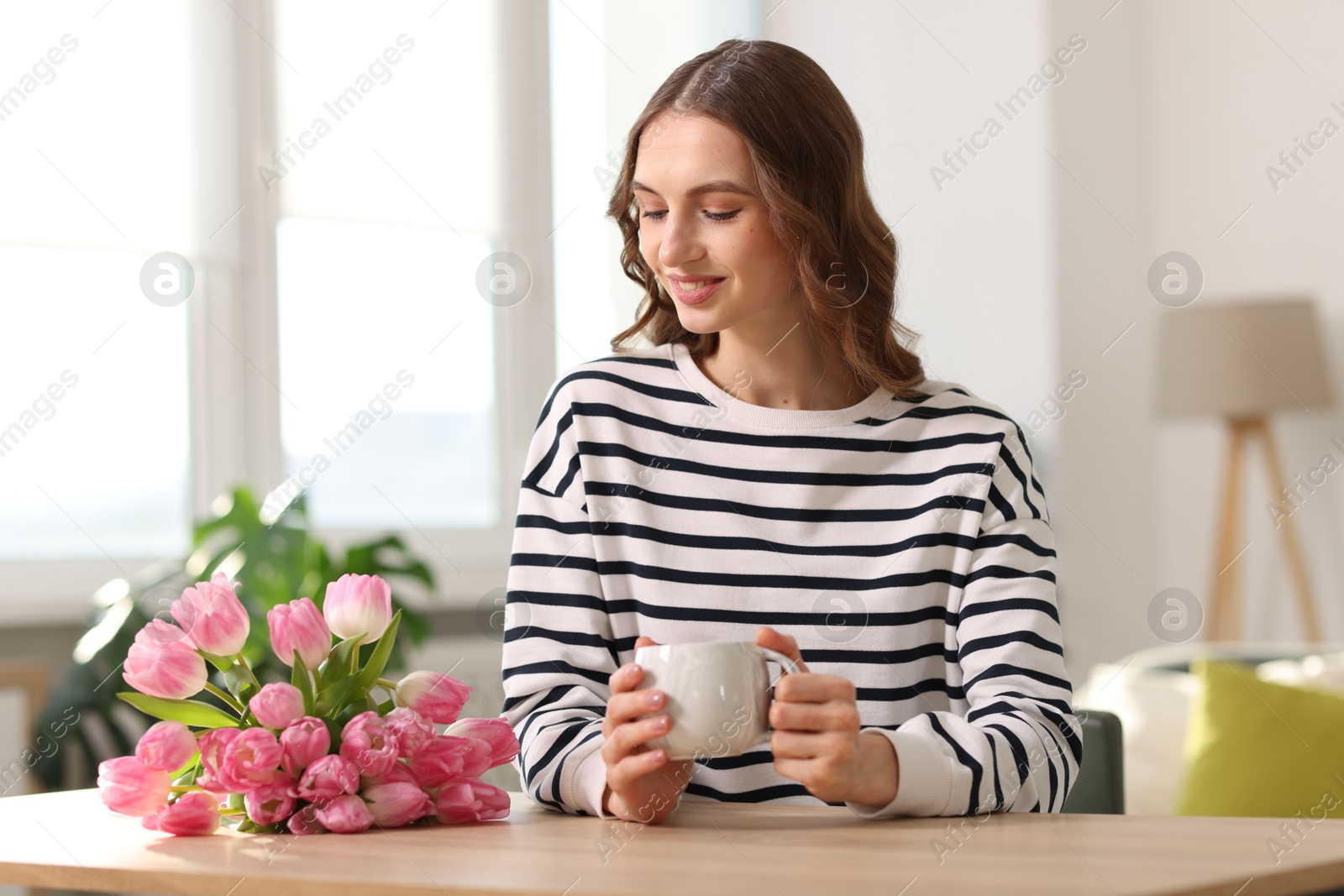 Photo of Smiling woman with bouquet of tulips at table indoors