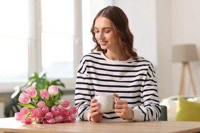 Photo of Smiling woman with bouquet of tulips at table indoors