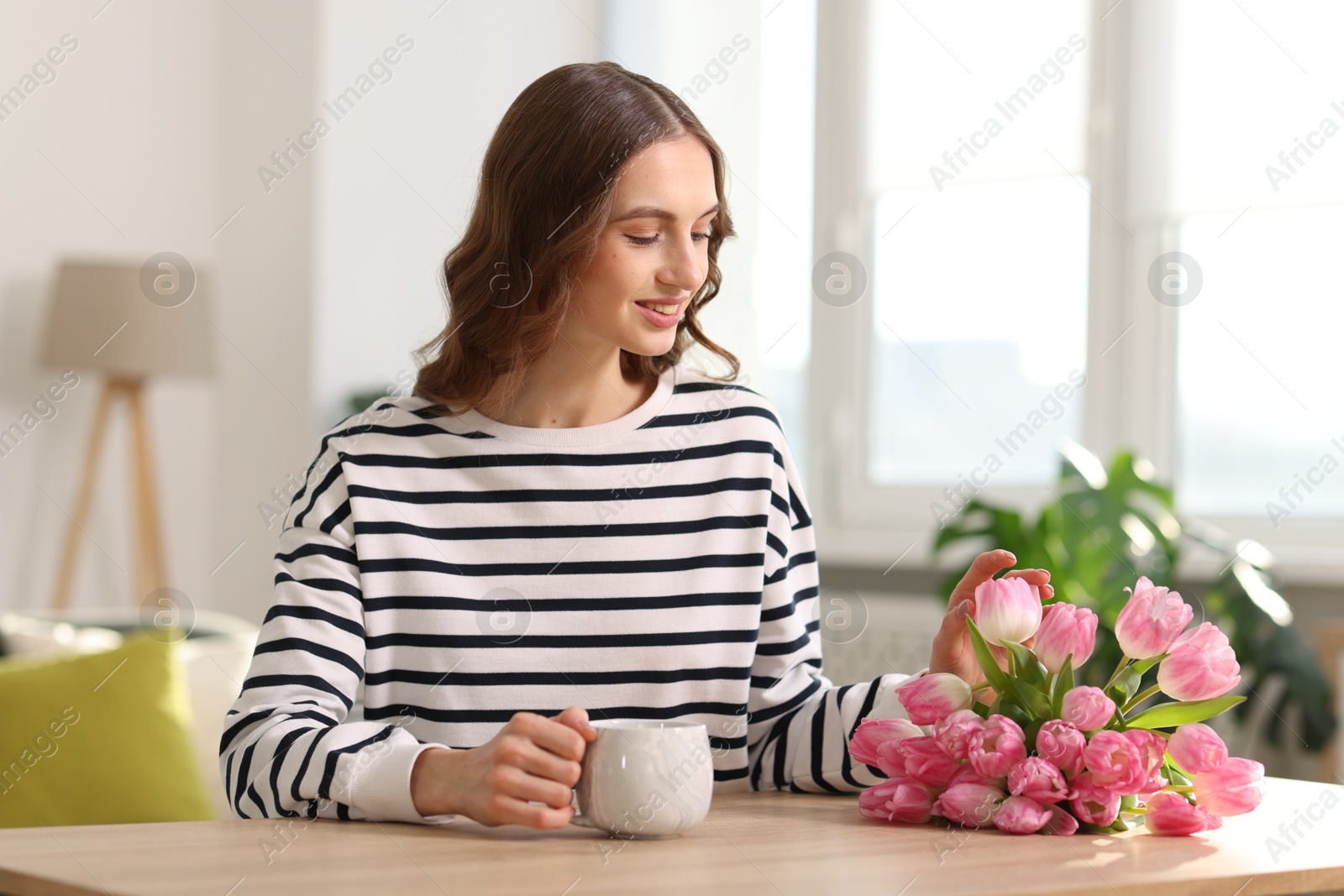 Photo of Smiling woman with bouquet of tulips at table indoors