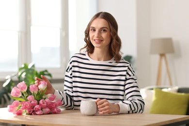 Photo of Smiling woman with bouquet of tulips at table indoors