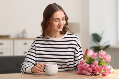 Photo of Smiling woman with bouquet of tulips at table indoors